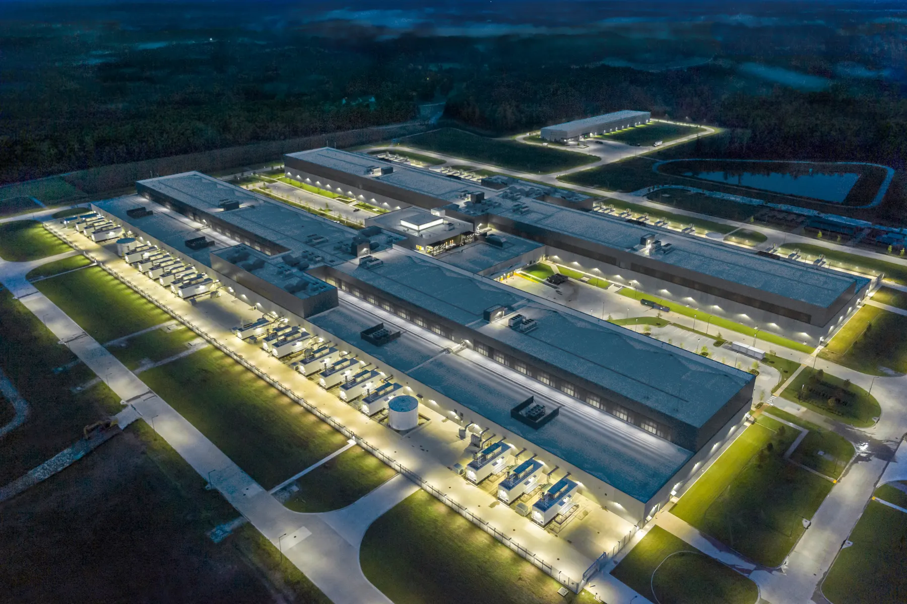 Aerial view of an illuminated industrial campus with roads, utility yards, and service buildings